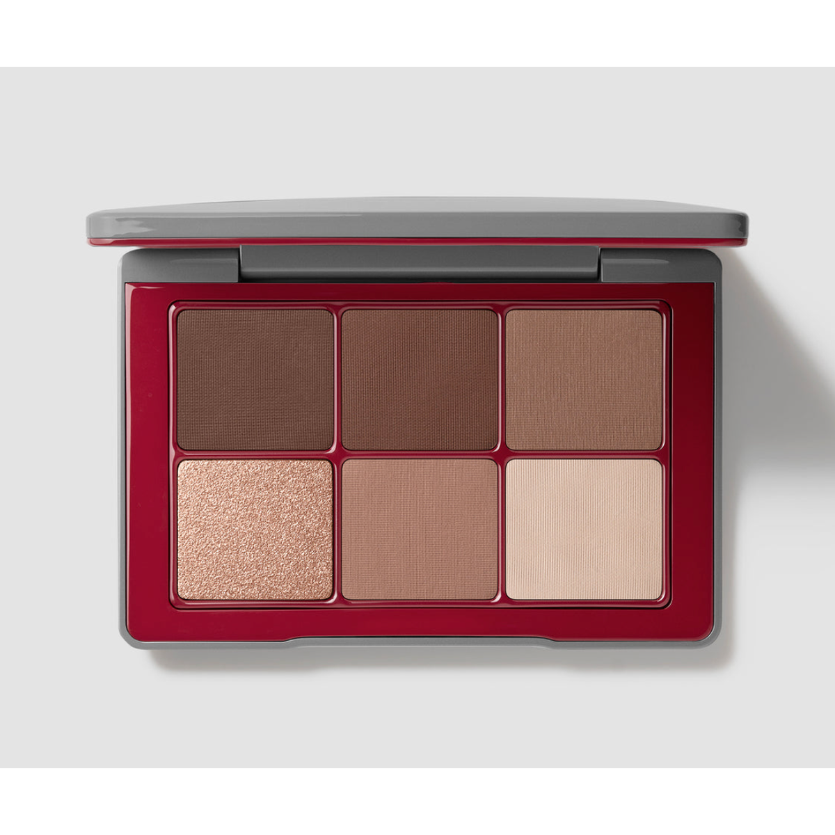 A six-pan eyeshadow palette in a deep red compact with a gray outer frame, shown open on a light gray background. The shades include three medium-to-dark browns, a shimmering champagne-beige, a warm tan, and a light beige.