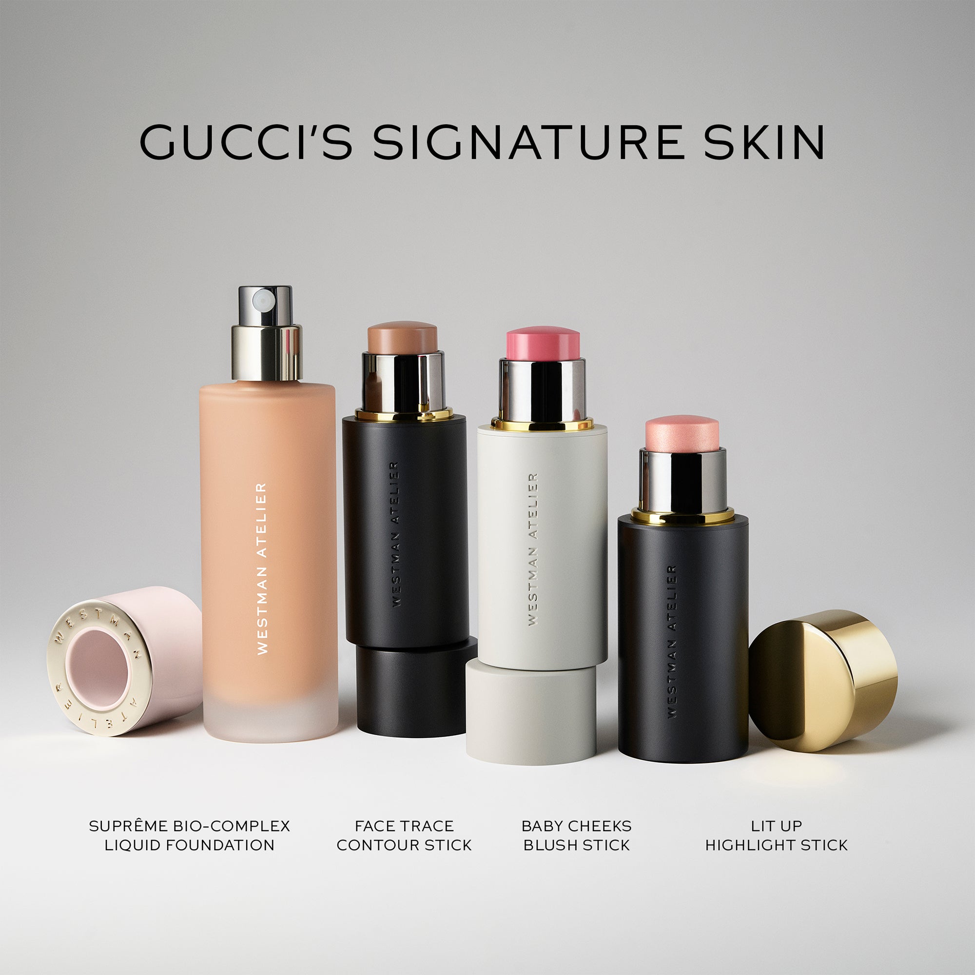 Four Westman Atelier cosmetic products arranged on a light gray background under the text 'GUCCI'S SIGNATURE SKIN.' The set includes a liquid foundation bottle, a black face trace contour stick, a white baby cheeks blush stick, and a black lit up highlight stick, with one cap lying on its side and one gold-toned highlight cap standing upright.