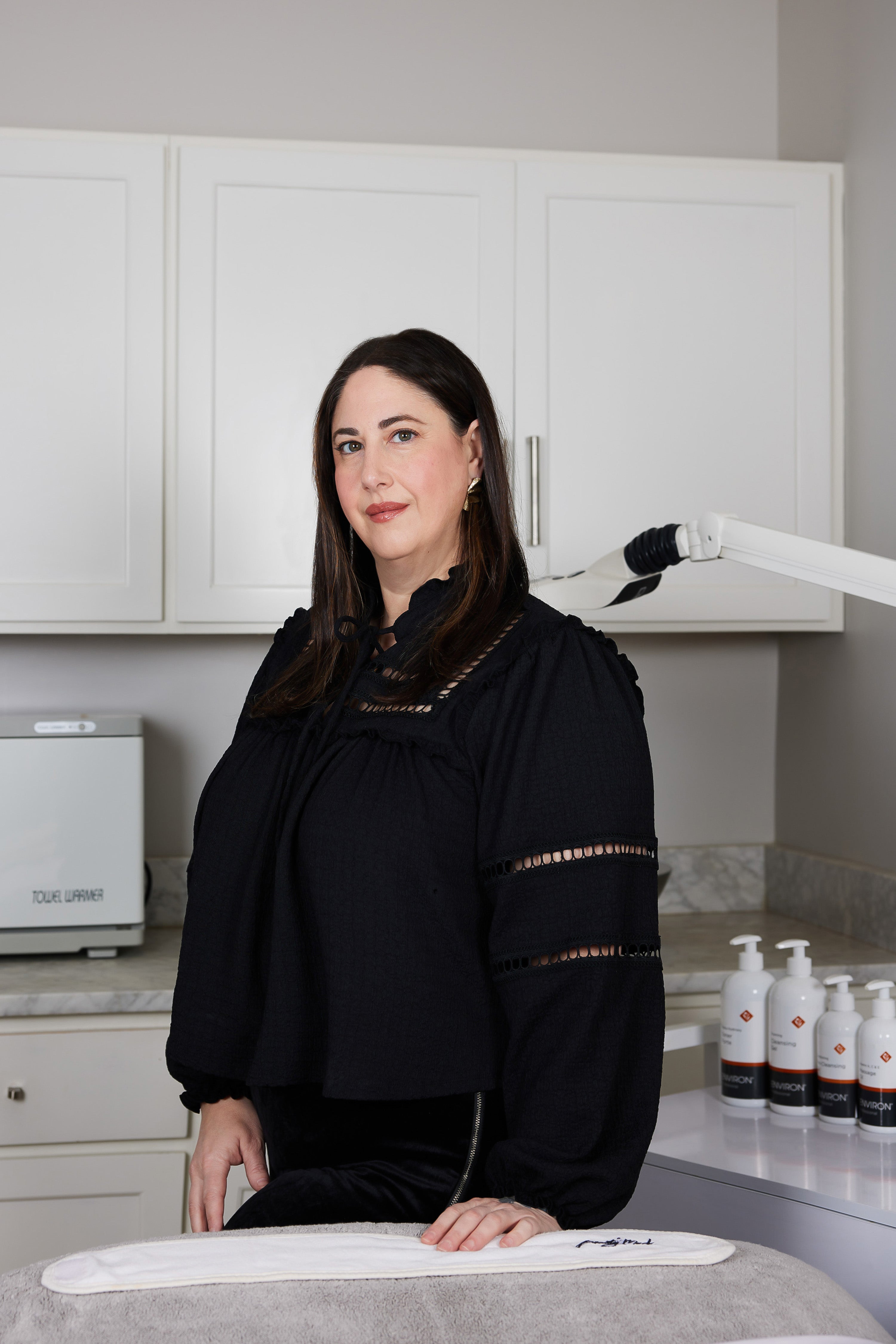 Vanessa, one of our Beauty Mark Estheticians standing and smiling at the camera wearing a black outfit 