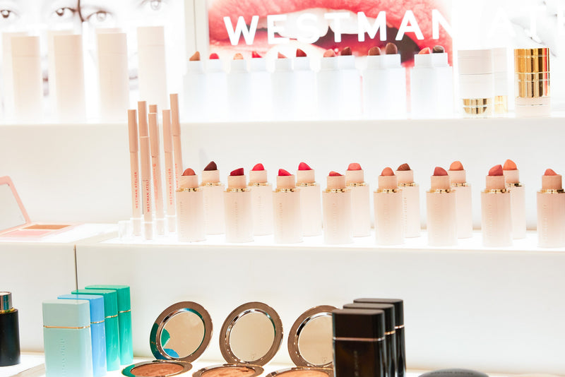 Bright display of multiple makeup products highlighting lip products with Westman Atelier branding in the background